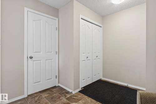 This entryway features tiled flooring, a white paneled door, and bi-fold closet doors - 215 1080 Mcconachie Boulevard, Edmonton, AB - Indoor Photo Showing Other Room