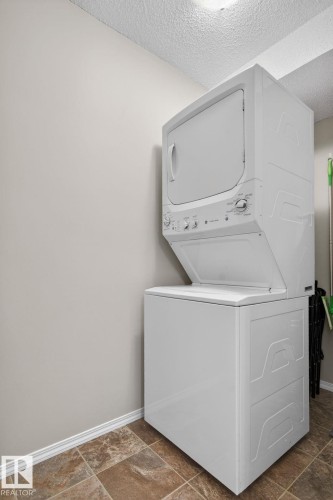 Laundry area featuring a stacked washer and dryer, tile flooring, and light-colored walls - 215 1080 Mcconachie Boulevard, Edmonton, AB - Indoor Photo Showing Laundry Room