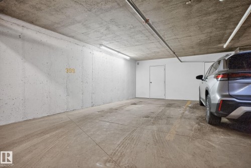 Spacious parking area with concrete walls and floor, featuring overhead lighting and a closed door - 215 1080 Mcconachie Boulevard, Edmonton, AB - Indoor Photo Showing Garage
