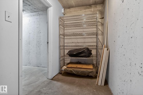 This area features concrete walls and flooring, with a metal shelving unit providing storage solutions - 215 1080 Mcconachie Boulevard, Edmonton, AB - Indoor Photo Showing Other Room