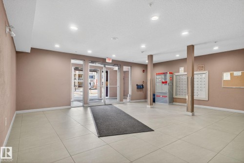 Well-lit entrance area featuring tile flooring, glass doors, and a bulletin board - 215 1080 Mcconachie Boulevard, Edmonton, AB - Indoor Photo Showing Other Room