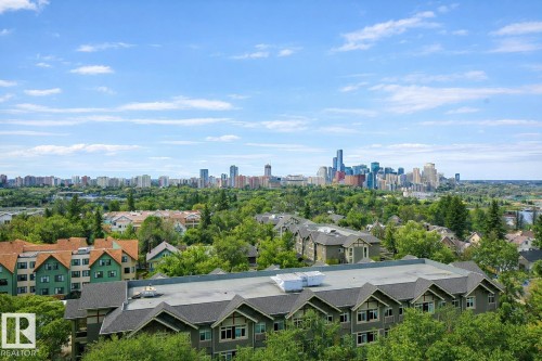 An aerial view showcasing the neighborhood's buildings and abundant green spaces, with a distant cityscape visible under a clear sky - 1004 11027 87 Avenue, Edmonton, AB - Outdoor With View