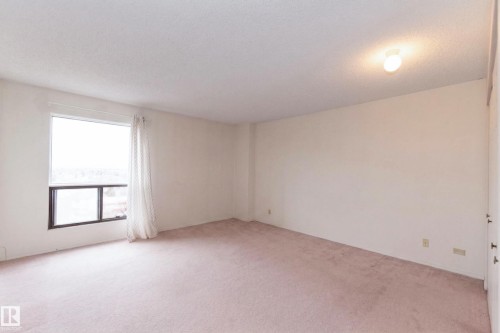 Spacious room featuring light-colored carpeting, a large window with vertical blinds and sheer curtains, and a ceiling-mounted light fixture - 1004 11027 87 Avenue, Edmonton, AB - Indoor Photo Showing Other Room