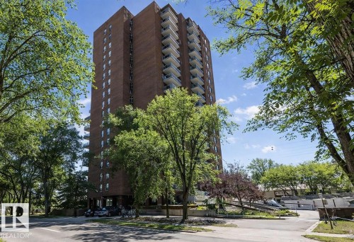 The property features a tall brick building with balconies and is surrounded by numerous trees and paved areas - 1004 11027 87 Avenue, Edmonton, AB - Outdoor