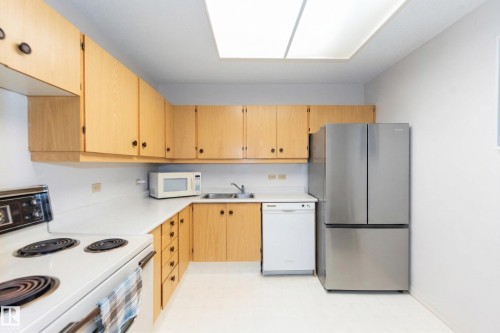 The kitchen features light wood cabinetry, white countertops, and a full suite of appliances including a stainless steel refrigerator, white dishwasher, and white electric range - 1004 11027 87 Avenue, Edmonton, AB - Indoor Photo Showing Kitchen