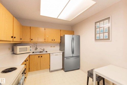 The kitchen features light-toned cabinetry, white countertops, a stainless steel refrigerator, and a skylight - 1004 11027 87 Avenue, Edmonton, AB - Indoor Photo Showing Kitchen