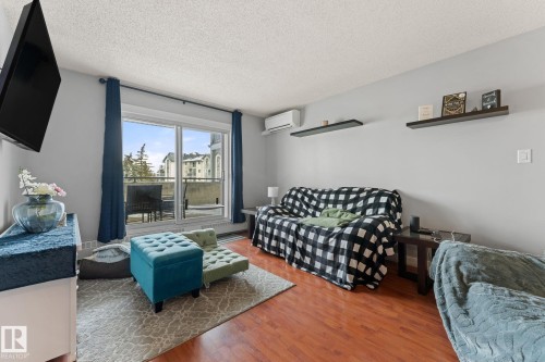 Living area featuring hardwood floors, light gray walls, a sliding glass door leading to a balcony, and decorative wall shelving - 208 6710 158 Avenue, Edmonton, AB - Indoor