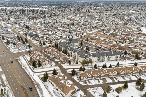 Aerial view showcasing the property within a developed residential area, featuring a multi-story building with a large parking area and surrounding townhomes - 208 6710 158 Avenue, Edmonton, AB - Outdoor With View