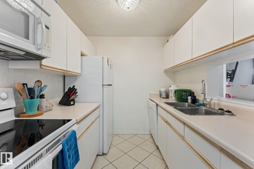 Efficient kitchen featuring white cabinetry, a double basin sink, and white appliances - 208 6710 158 Avenue, Edmonton, AB - Indoor Photo Showing Kitchen With Double Sink