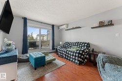 Living area featuring hardwood floors, light gray walls, a sliding glass door leading to a balcony, and decorative wall shelving - 