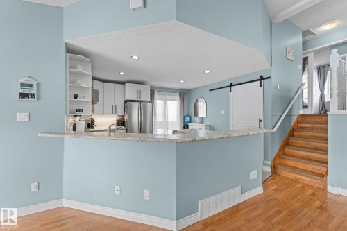 Kitchen featuring white cabinetry, stainless steel appliances, and a breakfast bar with a light-colored countertop - 7252 152C Avenue, Edmonton, AB - Indoor Photo Showing Kitchen