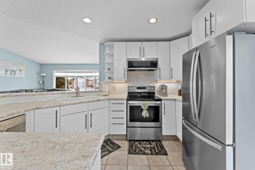 The kitchen features white cabinetry, light-colored countertops, stainless steel appliances, and tiled flooring - 7252 152C Avenue, Edmonton, AB - Indoor Photo Showing Kitchen