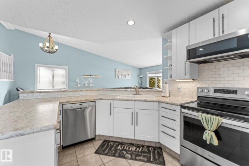 This kitchen features white cabinetry, stainless steel appliances including a dishwasher, oven, and microwave, and light-colored countertops - 7252 152C Avenue, Edmonton, AB - Indoor Photo Showing Kitchen