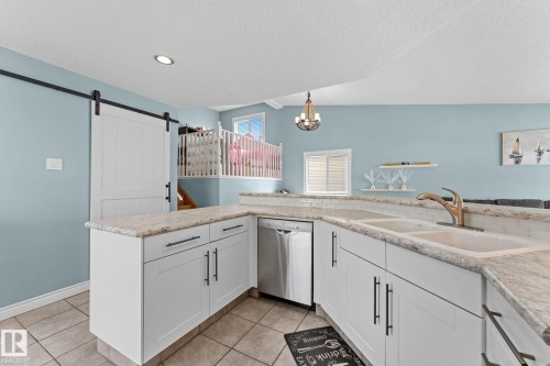 The kitchen features white cabinetry with dark hardware, light countertops, and a double sink with a gold-toned faucet - 7252 152C Avenue, Edmonton, AB - Indoor Photo Showing Kitchen