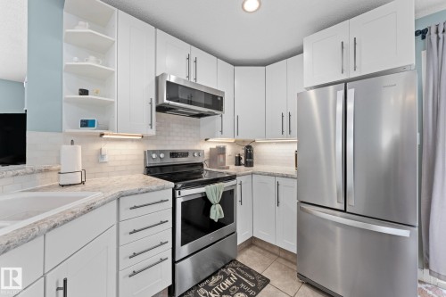 The kitchen features white cabinetry, stainless steel appliances, and light-colored countertops - 7252 152C Avenue, Edmonton, AB - Indoor Photo Showing Kitchen With Upgraded Kitchen