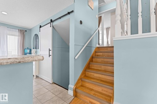 The property features a staircase with wooden treads and a white banister, alongside a white barn door on a black sliding track - 7252 152C Avenue, Edmonton, AB - Indoor Photo Showing Other Room