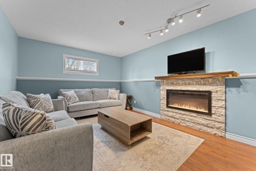 Living area featuring light blue walls, hardwood flooring, and a stone-clad fireplace with a mantel - 7252 152C Avenue, Edmonton, AB - Indoor Photo Showing Living Room With Fireplace