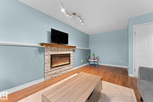 Living area featuring hardwood flooring, a stone-faced fireplace with a wooden mantel, and track lighting - 7252 152C Avenue, Edmonton, AB - Indoor Photo Showing Living Room With Fireplace