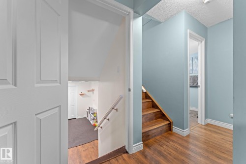 The property features natural wood flooring, a staircase with wooden treads, and walls painted in a light blue hue - 7252 152C Avenue, Edmonton, AB - Indoor Photo Showing Other Room