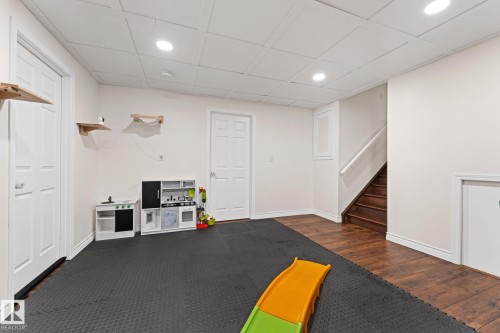 This versatile room features both dark wood-style flooring and a dark padded floor area, recessed lighting, and a staircase with a white railing - 7252 152C Avenue, Edmonton, AB - Indoor