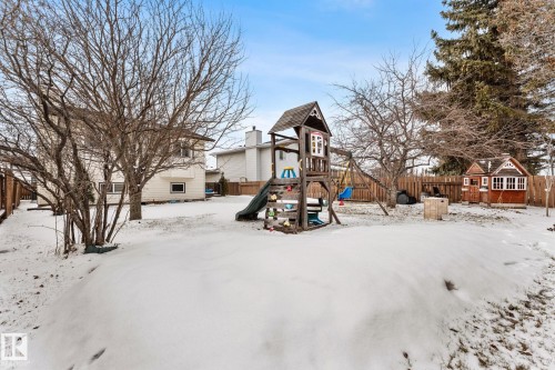 The property features a fenced backyard with a large play structure, a smaller playhouse, and several trees - 7252 152C Avenue, Edmonton, AB - Outdoor