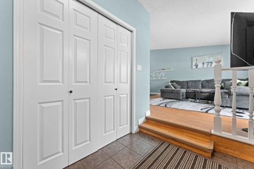 The property features a closet with bi-fold doors, tile flooring, and a hardwood floor area that steps down into a living space with light blue walls - 7252 152C Avenue, Edmonton, AB - Indoor Photo Showing Other Room