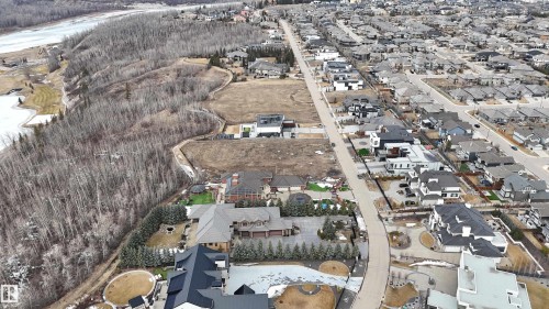Aerial view showcasing the neighborhood layout with numerous properties, streets, and an expanse of trees bordering a body of water - 24 Windermere Drive, Edmonton, AB 