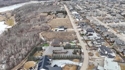 Aerial view showcasing the neighborhood layout with numerous properties, streets, and an expanse of trees bordering a body of water - 