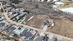 An aerial view showcasing a large, undeveloped parcel of land, surrounded by established residences and a nearby wooded area - 