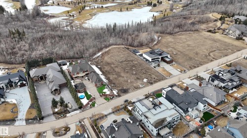 Aerial view of the property and its surrounding area, featuring a street, other properties, and a wooded area - 24 Windermere Drive, Edmonton, AB 