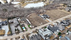 Aerial view of the property and its surrounding area, featuring a street, other properties, and a wooded area - 