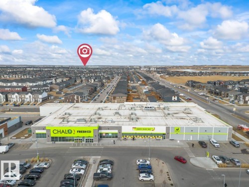 Aerial view highlighting the surrounding community, including a retail center with a grocery store, paved roads, and residential properties - 42 Corner Glen Manor Ne, Calgary, AB - Outdoor With View