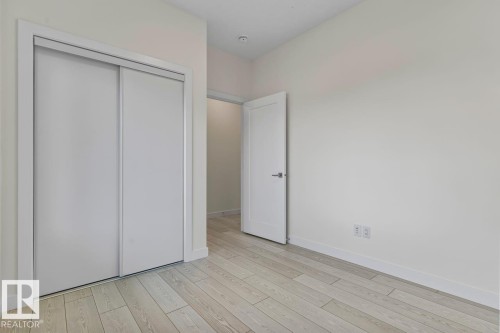 The room features light-colored plank flooring and white walls, complemented by a white door with a dark handle, and a closet with white sliding doors - 42 Corner Glen Manor Ne, Calgary, AB - Indoor Photo Showing Other Room