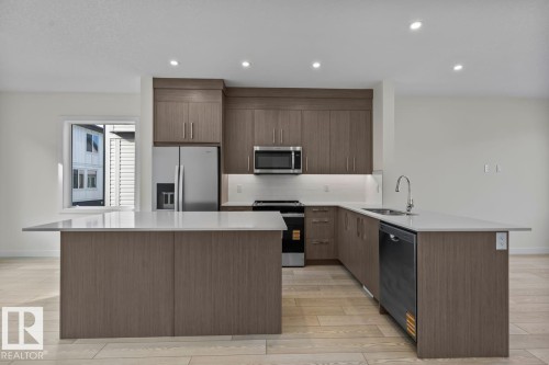 The property features a kitchen with wood-look cabinetry, stainless steel appliances, and light-colored countertops - 42 Corner Glen Manor Ne, Calgary, AB - Indoor Photo Showing Kitchen With Stainless Steel Kitchen With Upgraded Kitchen