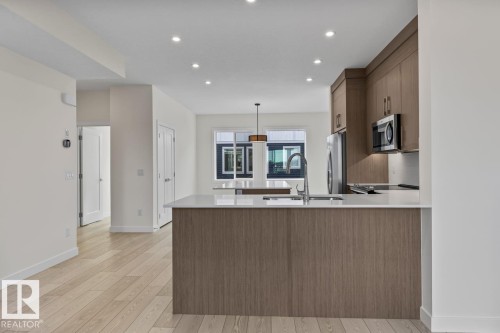 The kitchen features light wood cabinetry, stainless steel appliances, and a kitchen island with a sink and a modern faucet - 42 Corner Glen Manor Ne, Calgary, AB - Indoor Photo Showing Kitchen