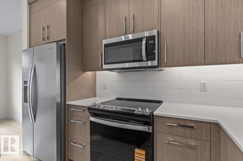 The kitchen features wood-look cabinetry, a stainless steel refrigerator, a stainless steel microwave, and a black electric range - 42 Corner Glen Manor Ne, Calgary, AB - Indoor Photo Showing Kitchen