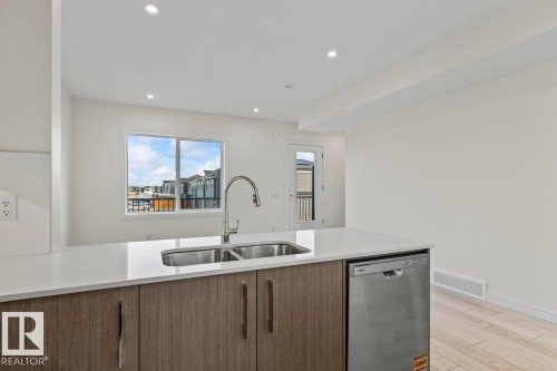 The kitchen features an island with a double stainless steel sink, a modern faucet, and a dishwasher - 42 Corner Glen Manor Ne, Calgary, AB - Indoor Photo Showing Kitchen With Double Sink