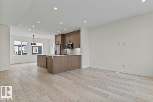 Open concept living space featuring light-toned wood flooring, recessed lighting, and a modern kitchen with a large island, stainless steel appliances, and wood cabinetry - 42 Corner Glen Manor Ne, Calgary, AB - Indoor Photo Showing Kitchen