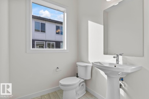 The bathroom features a white pedestal sink with a chrome faucet, a toilet, and a window providing natural light - 42 Corner Glen Manor Ne, Calgary, AB - Indoor Photo Showing Bathroom