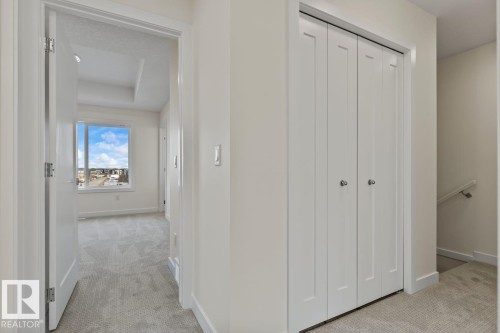 Hallway featuring light-colored carpeting, white walls, and a view into a room with a large window - 42 Corner Glen Manor Ne, Calgary, AB - Indoor Photo Showing Other Room