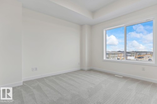 This room features light gray patterned carpeting, white walls, and a large window providing views of the surrounding neighborhood and sky - 42 Corner Glen Manor Ne, Calgary, AB - Indoor Photo Showing Other Room