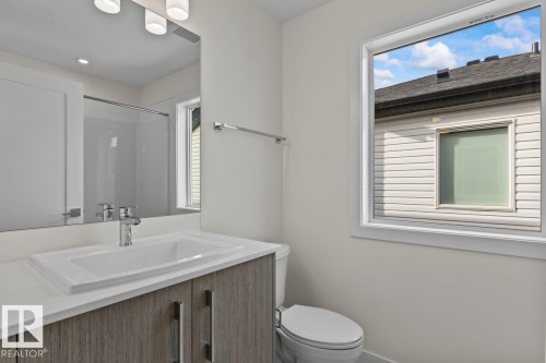 The bathroom features a vanity with a white countertop and a rectangular sink, a toilet, and a window providing natural light - 42 Corner Glen Manor Ne, Calgary, AB - Indoor Photo Showing Bathroom