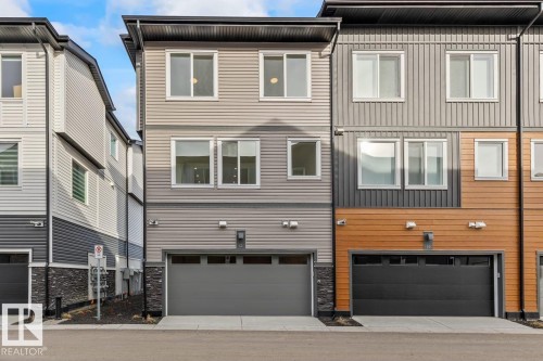 Contemporary style townhouse featuring light gray siding, a dark gray garage door, and a stone facade detail - 42 Corner Glen Manor Ne, Calgary, AB - Outdoor