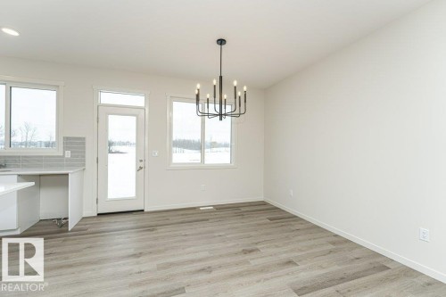 This bright and inviting room features light-toned flooring, white walls, and a contemporary black chandelier - 6298 180 Avenue, Edmonton, AB - Indoor Photo Showing Other Room