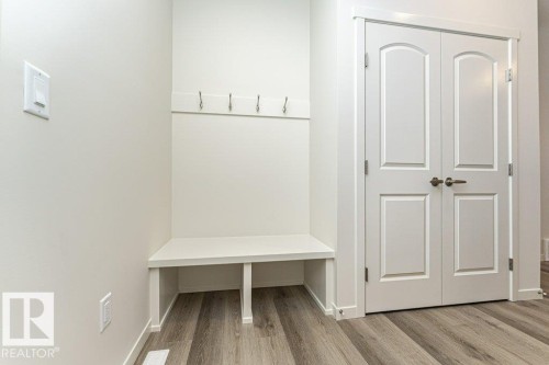 Entryway featuring light-colored walls, wood-style flooring, a built-in bench with coat hooks, and a set of double doors with dark hardware - 6298 180 Avenue, Edmonton, AB - Indoor Photo Showing Other Room