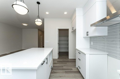 Modern kitchen featuring a large island with a white countertop and black hardware, white cabinetry, a stylish subway tile backsplash, and recessed lighting - 6298 180 Avenue, Edmonton, AB - Indoor Photo Showing Kitchen