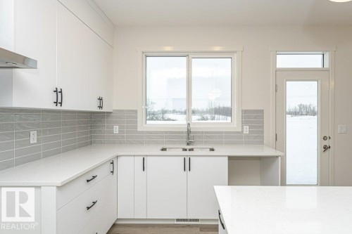 The kitchen features white cabinetry, light-colored countertops, a grey subway tile backsplash, and a window above the sink - 6298 180 Avenue, Edmonton, AB - Indoor Photo Showing Kitchen With Double Sink