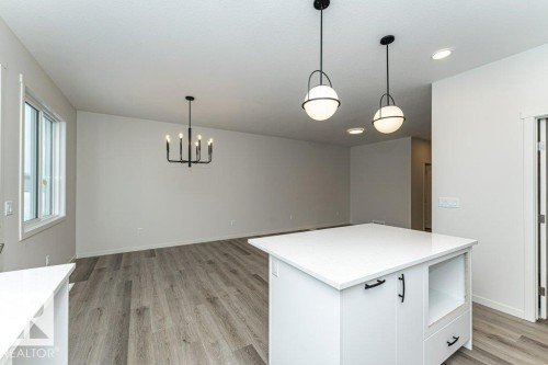 Open concept living space featuring light-colored flooring, a kitchen island with a white countertop and black hardware, and contemporary light fixtures - 6298 180 Avenue, Edmonton, AB - Indoor