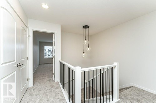 The property features a staircase with white newel posts and black balusters, illuminated by a contemporary pendant light fixture - 6298 180 Avenue, Edmonton, AB - Indoor Photo Showing Other Room