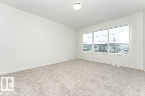 This room features light-colored walls, carpeted flooring, and a large window providing views of the neighborhood - 6298 180 Avenue, Edmonton, AB - Indoor Photo Showing Other Room